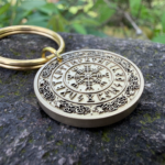 Keychain with Vegvisir Norse compass engraving on stone surface, surrounded by lush greenery.