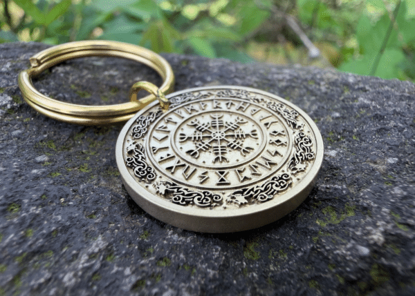 Keychain with Vegvisir Norse compass engraving on stone surface, surrounded by lush greenery.