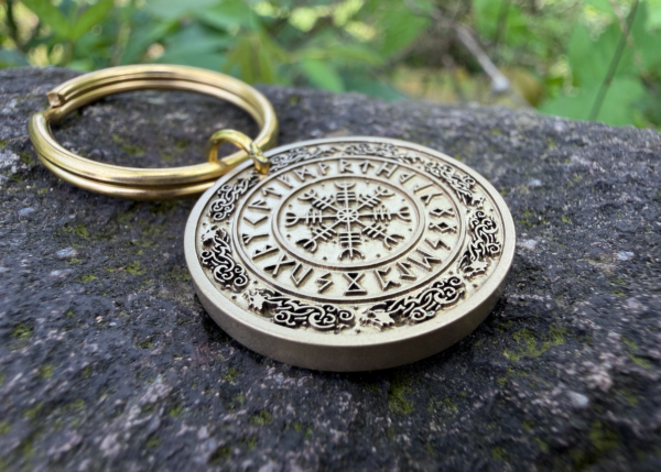 Keychain with Vegvisir Norse compass engraving on stone surface, surrounded by lush greenery.