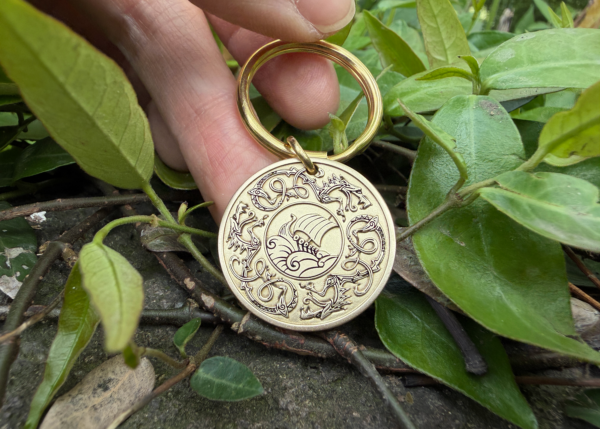 Intricate circular keychain with ocean wave engraving, surrounded by animal designs, placed on green leaves.
