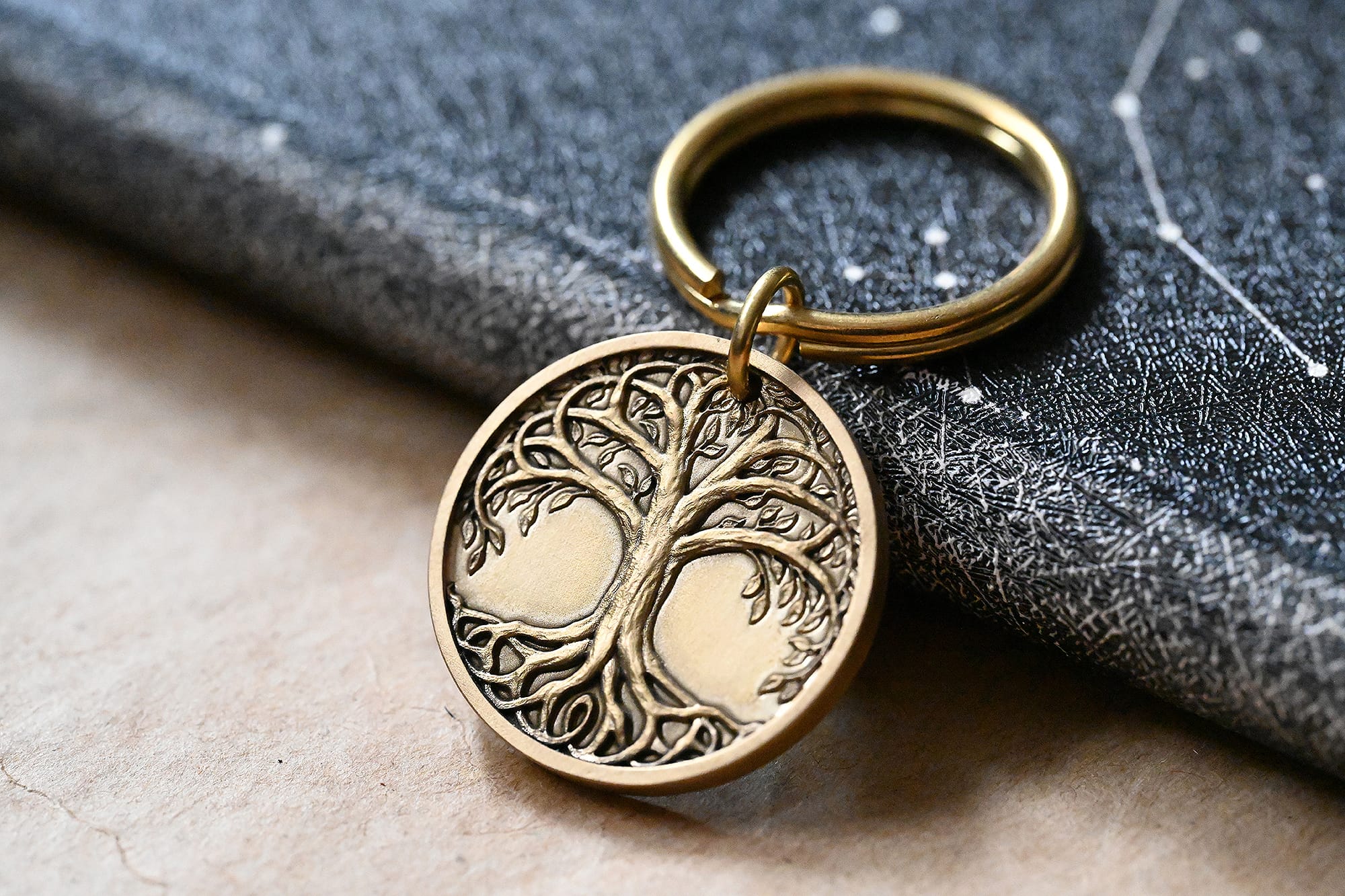 Bronze keychain with intricate Tree of Life engraving, resting on a textured book cover.