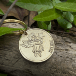 Gold angel keychain on wood amidst green leaves, perfect for gifts and personalization.