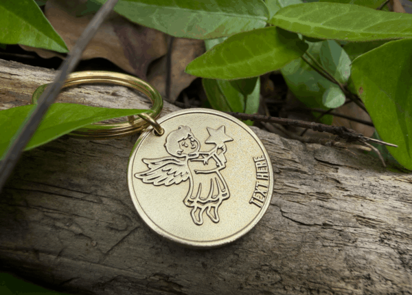 Gold angel keychain on wood amidst green leaves, perfect for gifts and personalization.