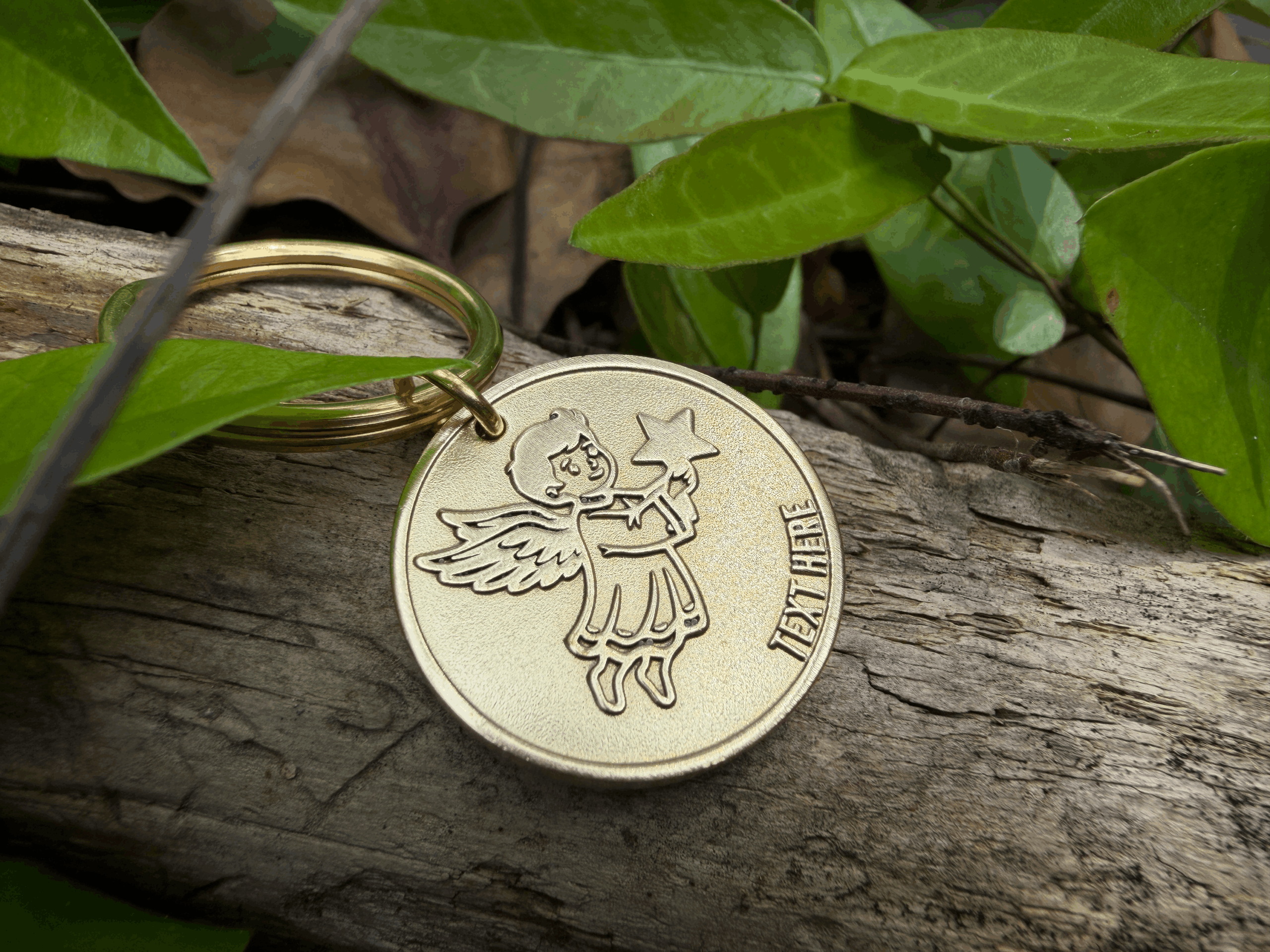 Gold angel keychain on wood amidst green leaves, perfect for gifts and personalization.