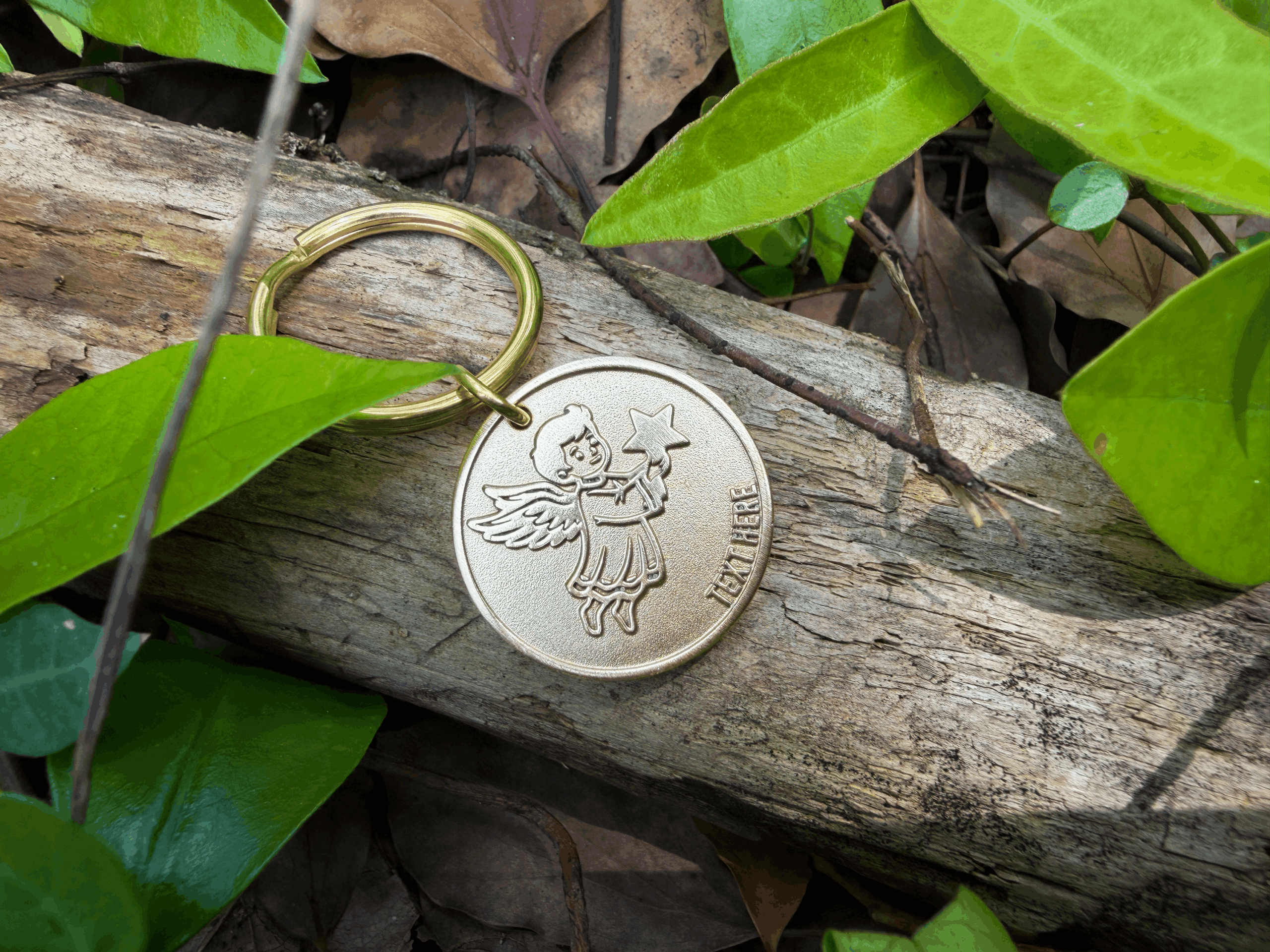 Gold angel keychain on a log surrounded by green leaves in a natural setting.