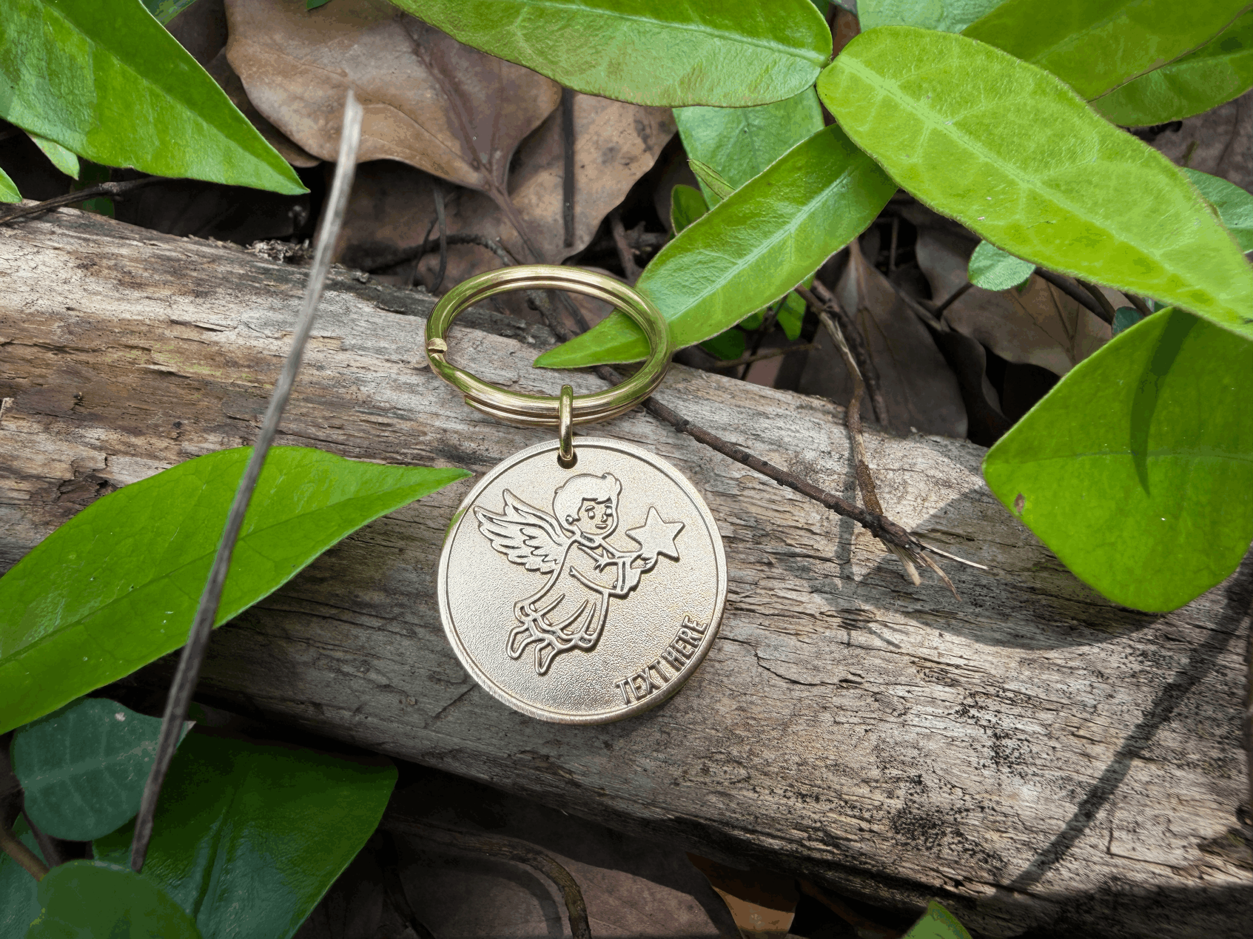 Angel keychain on a log surrounded by green leaves in a natural setting.
