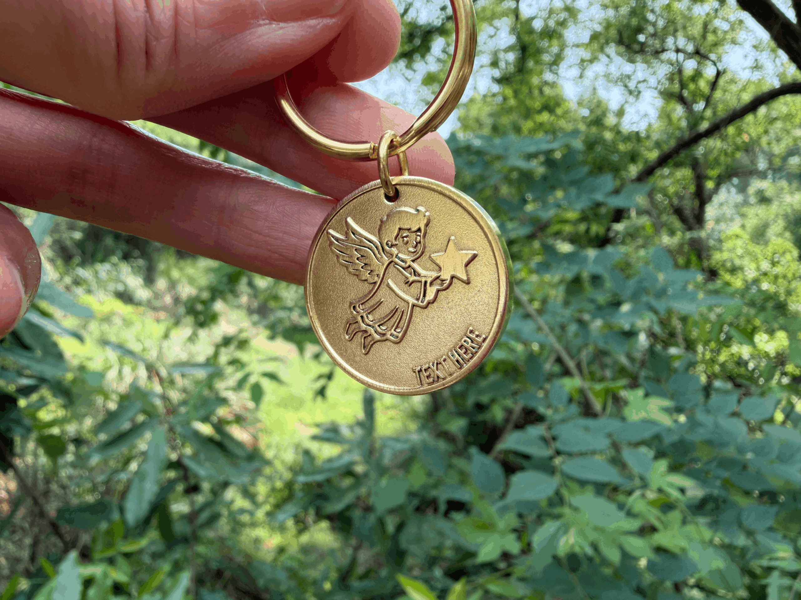 Angel-themed gold keychain with star design held against a lush green forest backdrop.