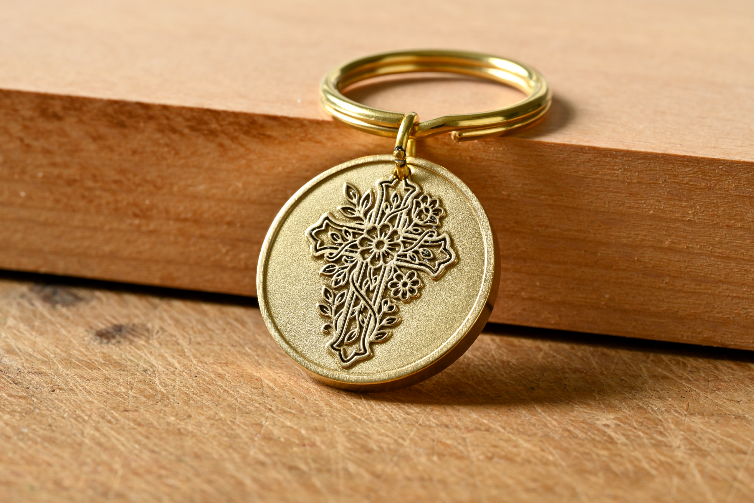 Gold keychain with a circular medallion featuring an embossed floral cross design