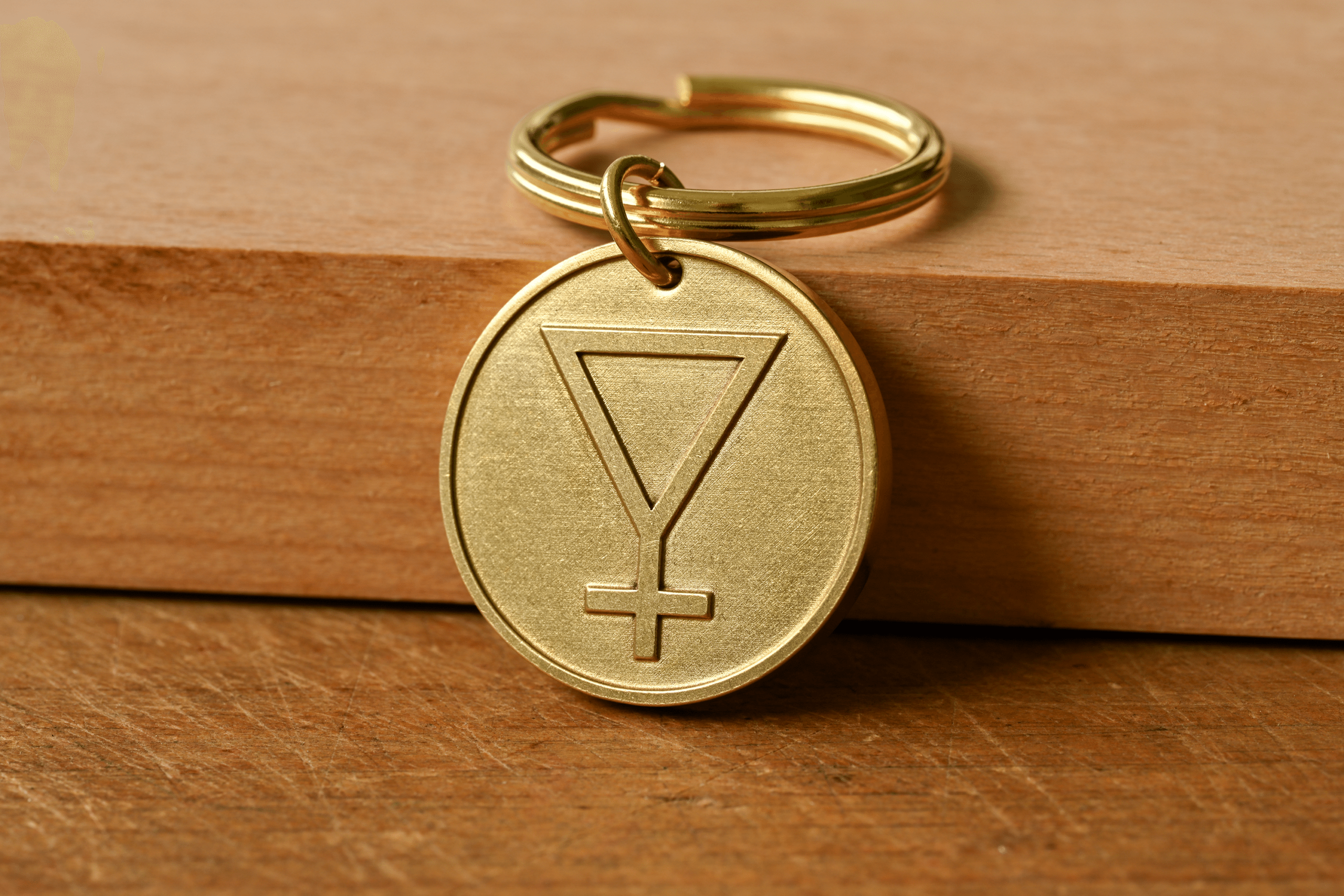 Brass circular keychain tag engraved with an inverted triangle and cross symbol