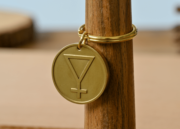 Gold circular pendant engraved with an inverted triangle and cross symbol on a wooden stand
