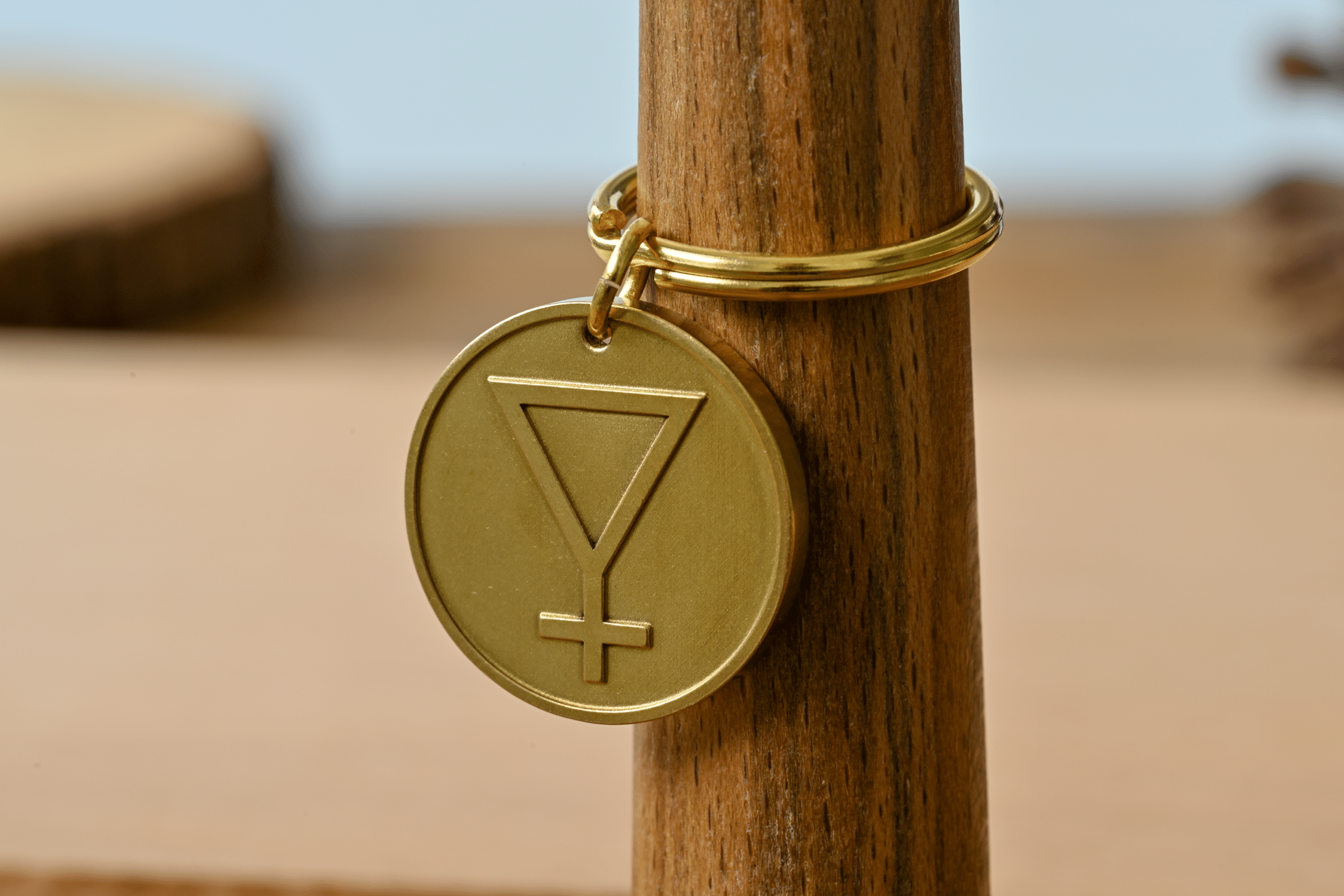 Gold circular pendant engraved with an inverted triangle and cross symbol on a wooden stand