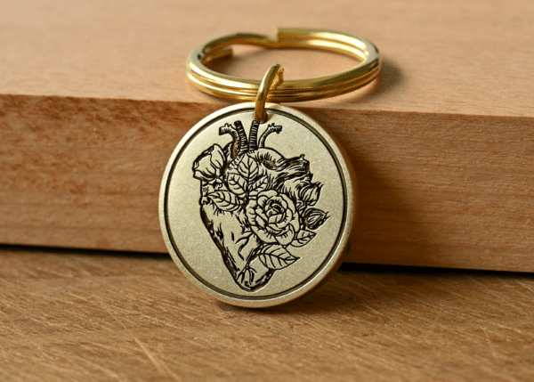 Circular brass keychain tag engraved with an anatomical heart intertwined with blooming roses