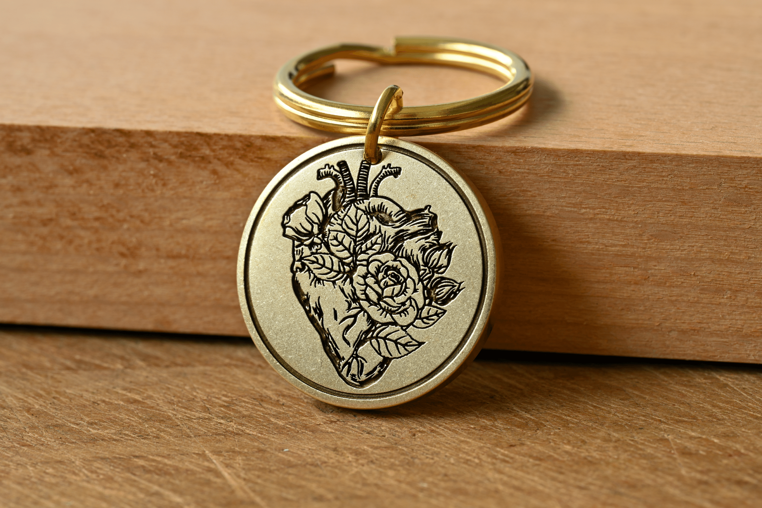 Circular brass keychain tag engraved with an anatomical heart intertwined with blooming roses