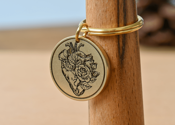 Round gold keychain medallion engraved with an anatomical heart and blooming roses