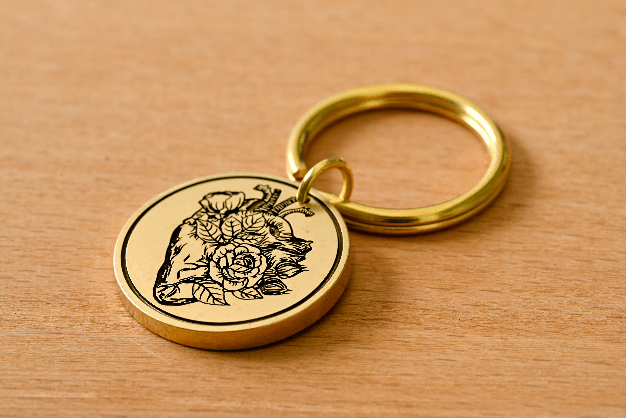 Gold circular brass keychain engraved with an anatomical heart and blooming roses