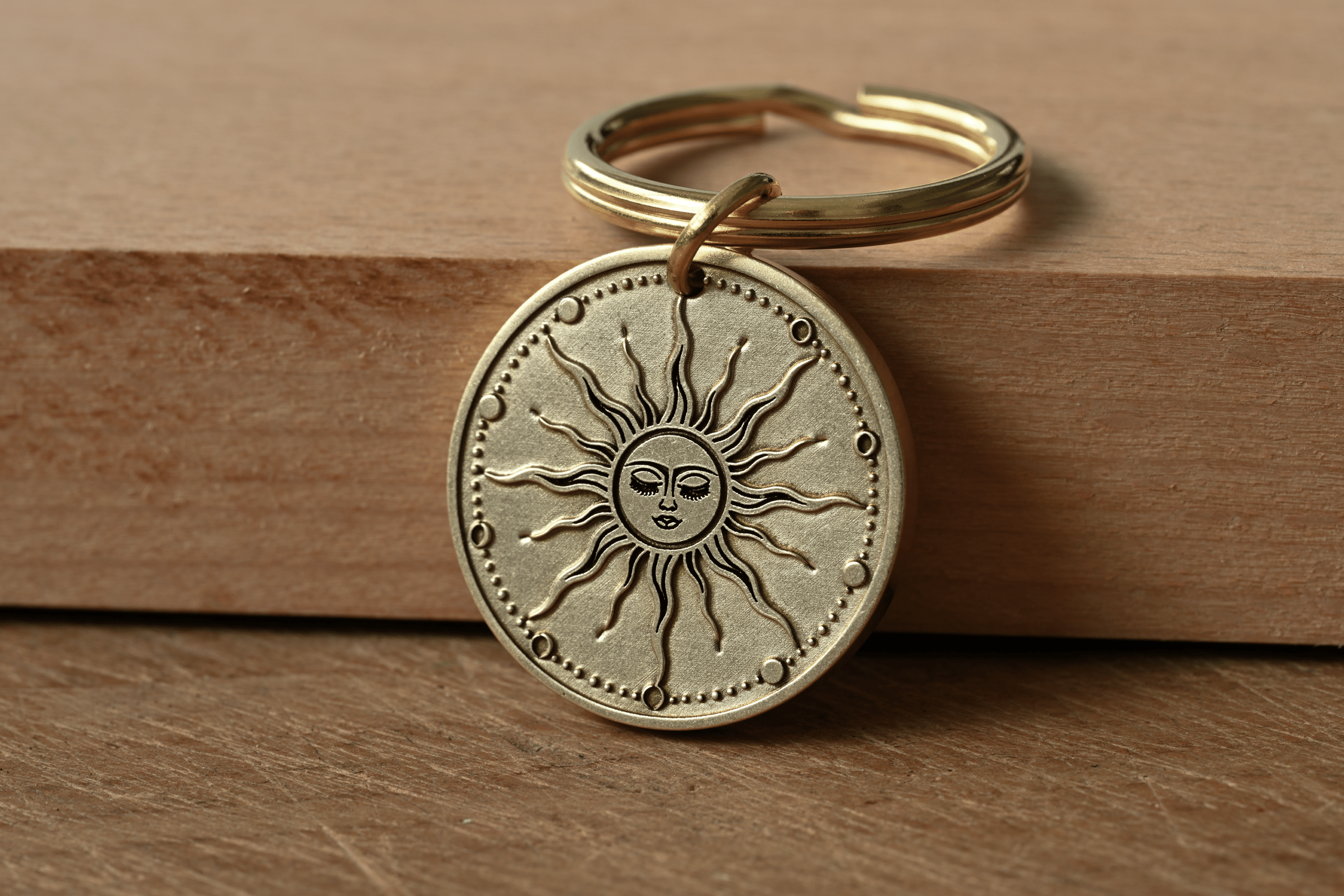 Brass key ring with a circular pendant featuring an engraved celestial sun with a face and wavy rays