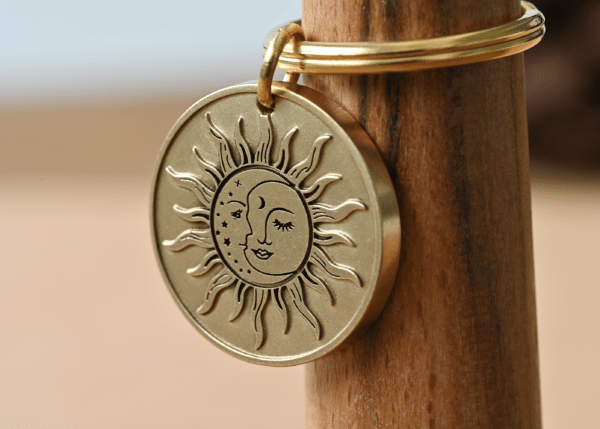 Round brass keychain pendant engraved with a celestial sun and crescent moon design