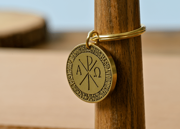 Gold keyring with a circular Chi Rho medallion featuring Alpha and Omega symbols and border inscription