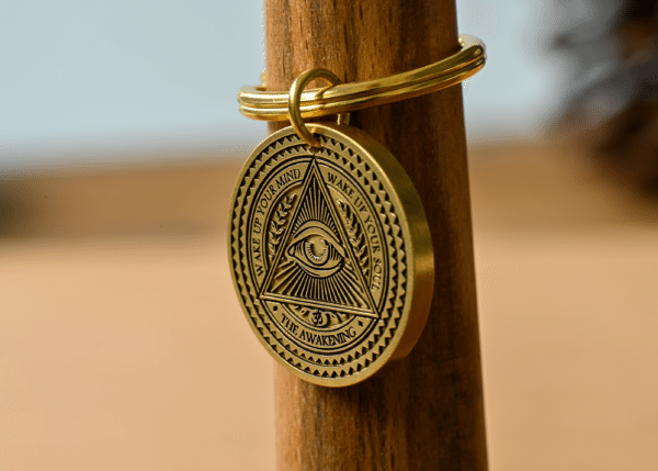 Gold medallion keychain featuring an Eye of Providence with text reading Wake Up Your Mind, Wake Up Your Soul, The Awakening