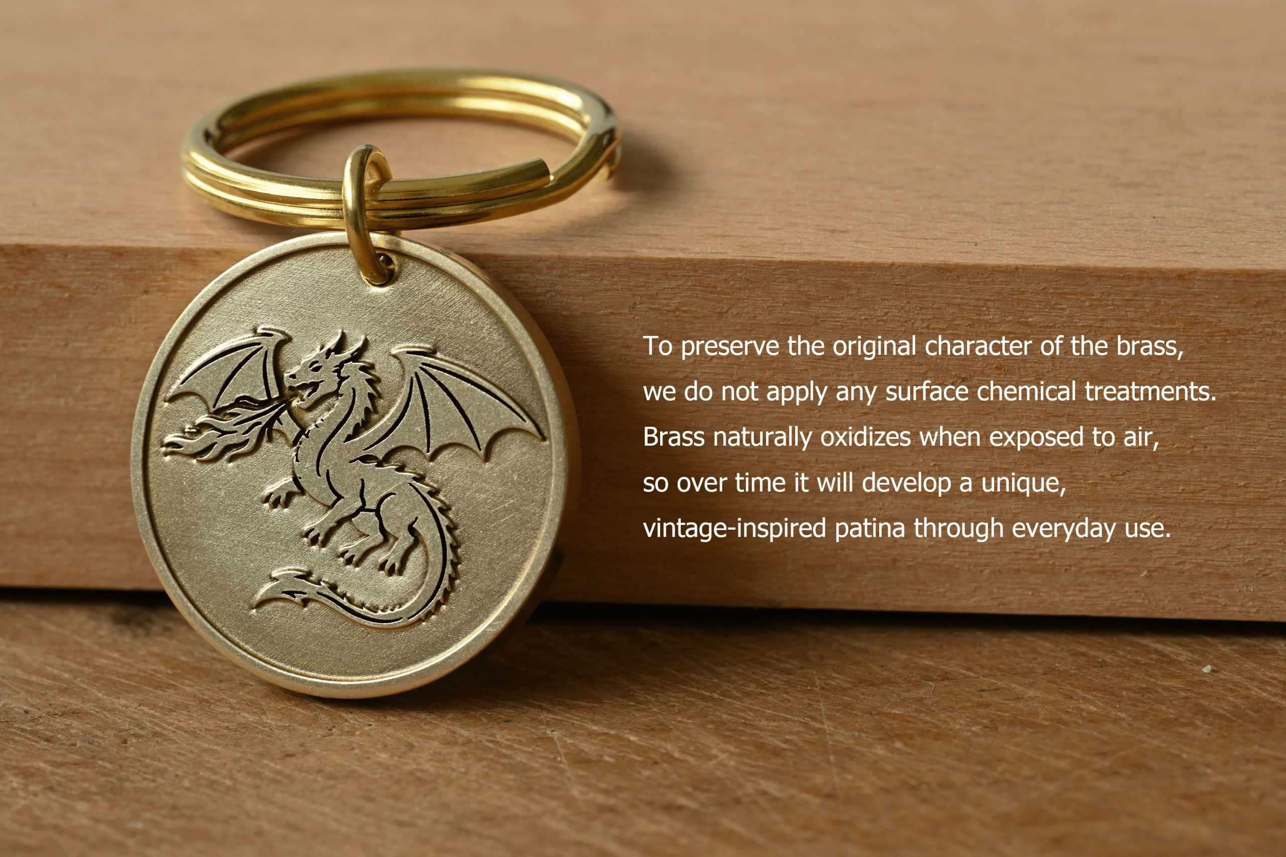 Brass dragon medallion keychain resting on wood alongside text: To preserve the original character of the brass, we do not apply any surface chemical treatments. Brass naturally oxidizes when exposed to air, so over time it will develop a unique, vintage-inspired patina through everyday use