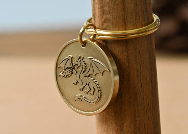 Brass circular keychain tag engraved with a fire-breathing dragon