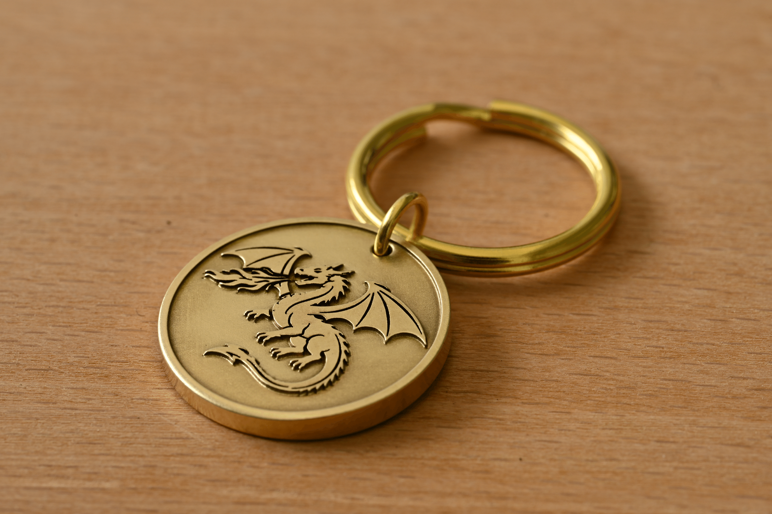 Gold keychain featuring a circular brass tag engraved with a fire-breathing dragon, resting on a wooden surface