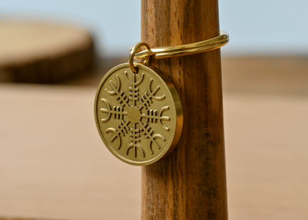 Gold brass keychain engraved with the Norse Helm of Awe symbol hanging on a wooden peg