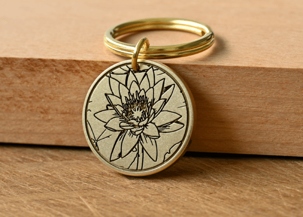 Round brass keychain with an engraved lotus flower design resting on a wooden surface