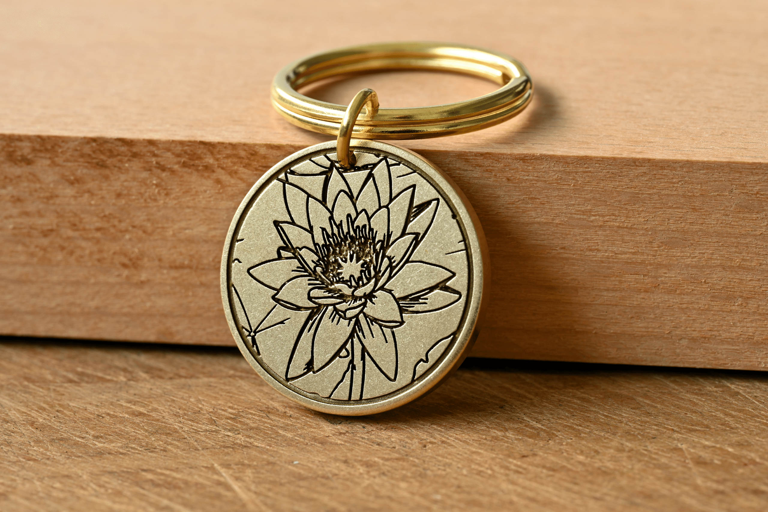 Round brass keychain with an engraved lotus flower design resting on a wooden surface