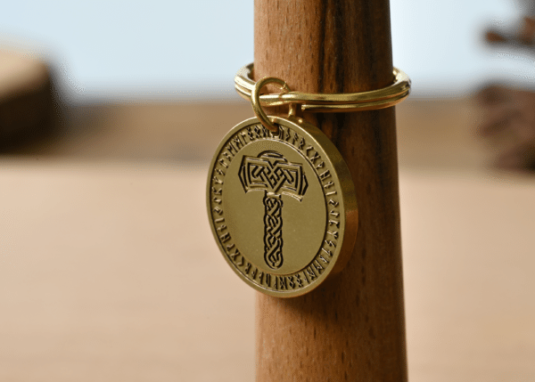 Gold circular keychain pendant engraved with Thor's hammer, Mjolnir, encircled by runic letters