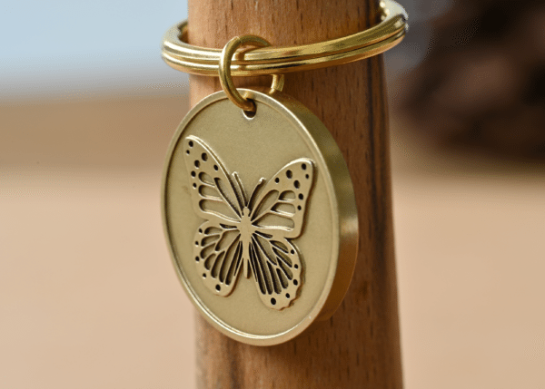 Round brass keychain pendant featuring a detailed butterfly design hanging on a key ring