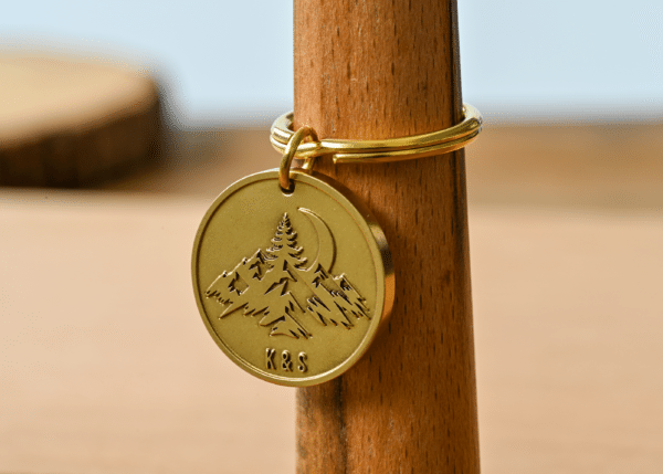 Round brass keychain tag engraved with a mountain landscape, crescent moon, and the initials K&S