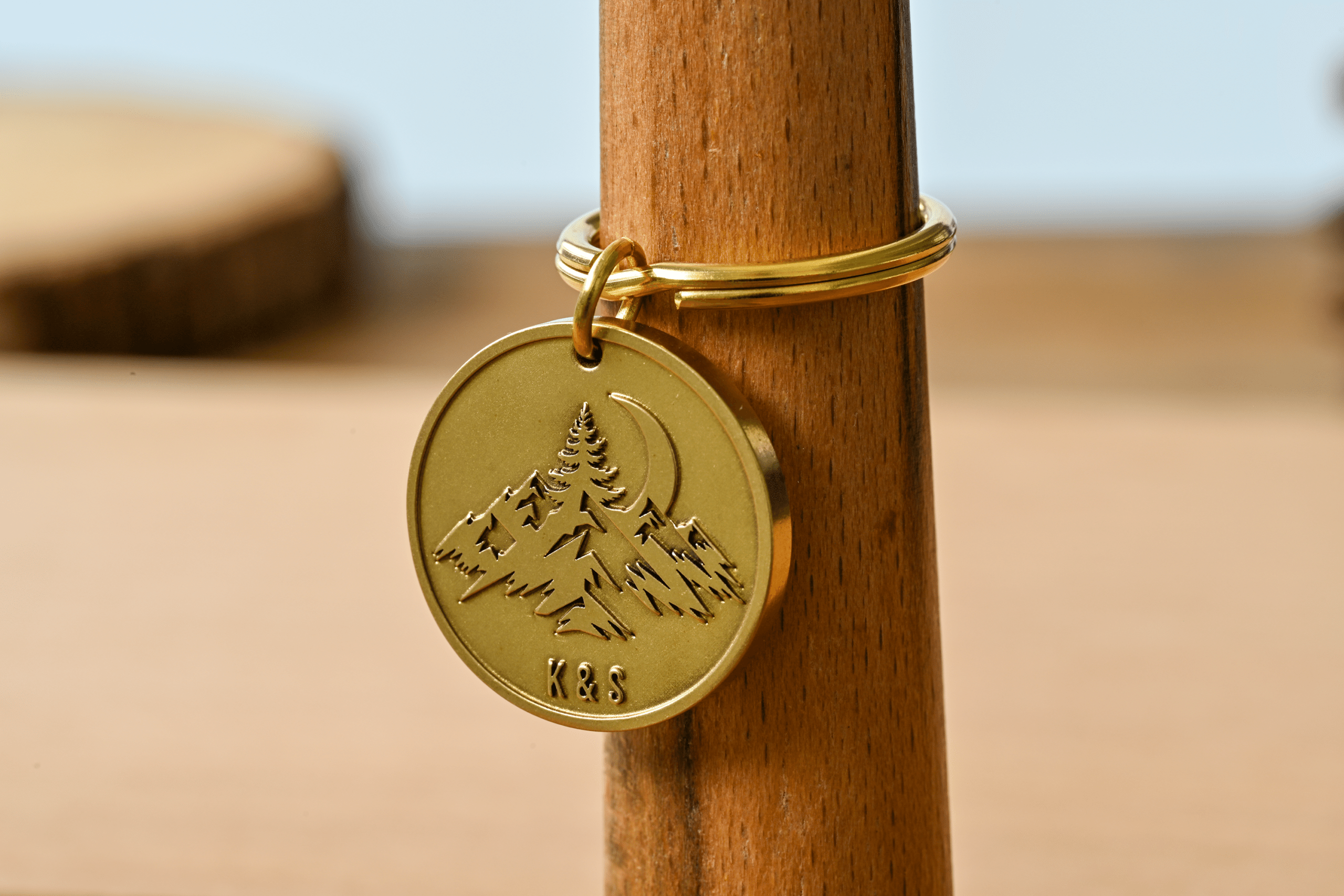Round brass keychain tag engraved with a mountain landscape, crescent moon, and the initials K&S