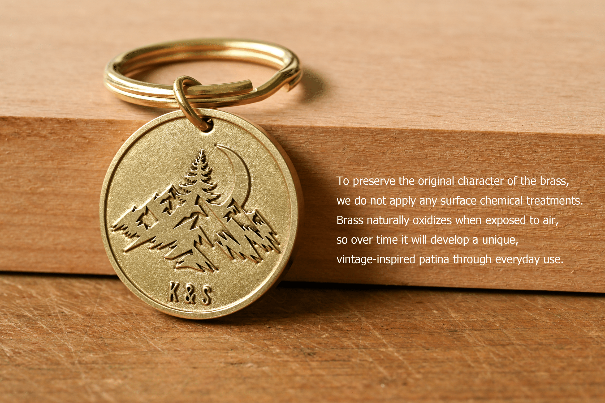 Round brass keychain engraved with a mountain scene and the initials K & S, next to text explaining that untreated brass naturally oxidizes over time to develop a unique vintage patina