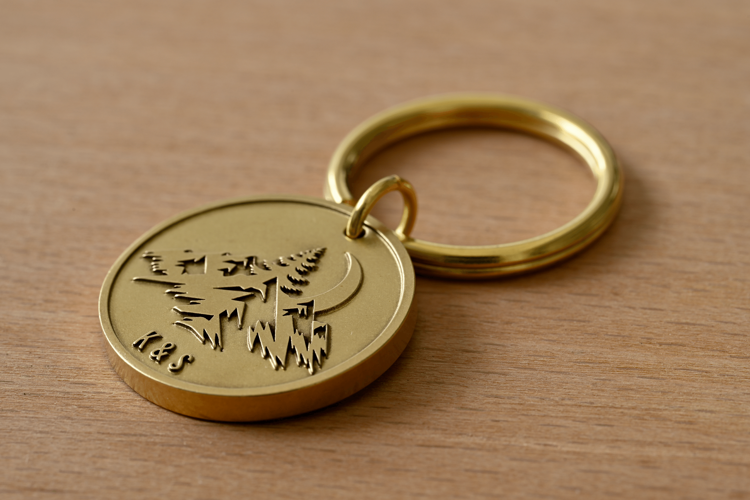 Brass keychain engraved with a mountain landscape, crescent moon, pine trees, and the initials K&S