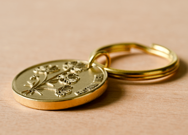 Gold oval keychain tag engraved with flowers and text reading CUSTOM HERE