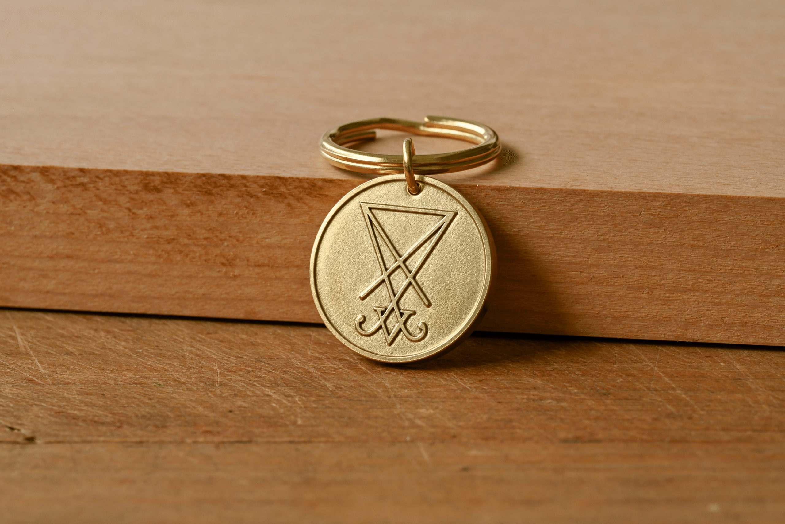 Round brass keychain pendant engraved with the Sigil of Lucifer resting on a wooden surface