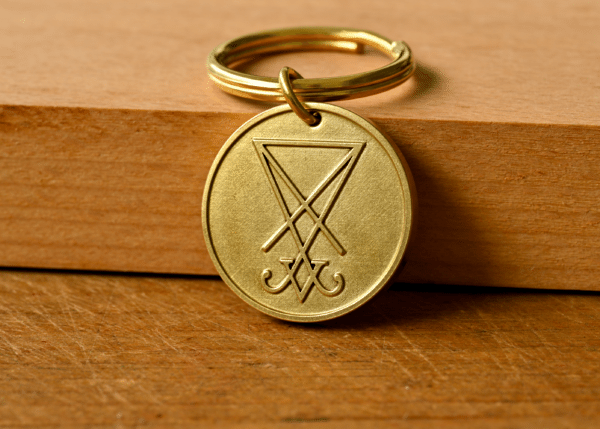 Round brass keychain pendant engraved with the Sigil of Lucifer on a wooden surface
