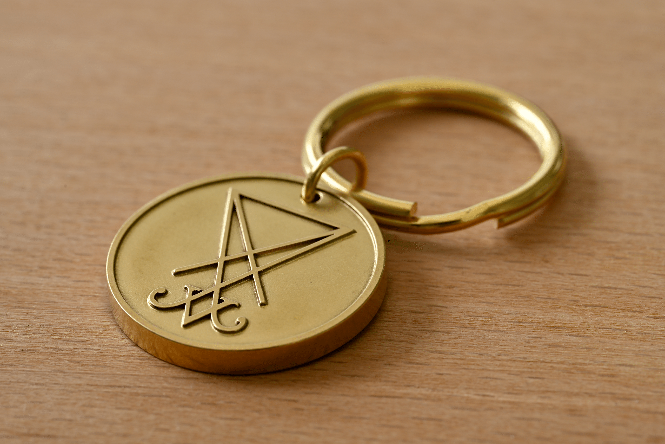 Brass keychain medallion engraved with the Sigil of Lucifer resting on a wooden surface