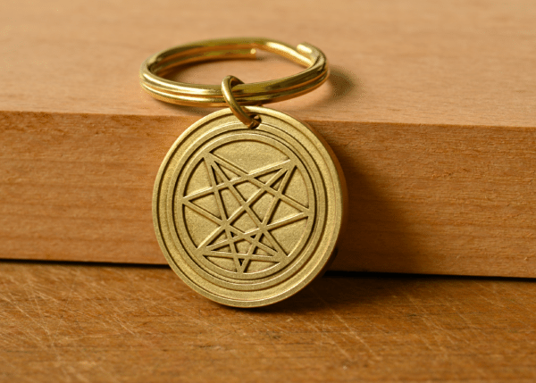 Brass keychain medallion engraved with an intricate star symbol resting against a wooden block