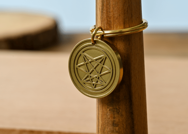 Gold circular keychain pendant with an engraved geometric star emblem
