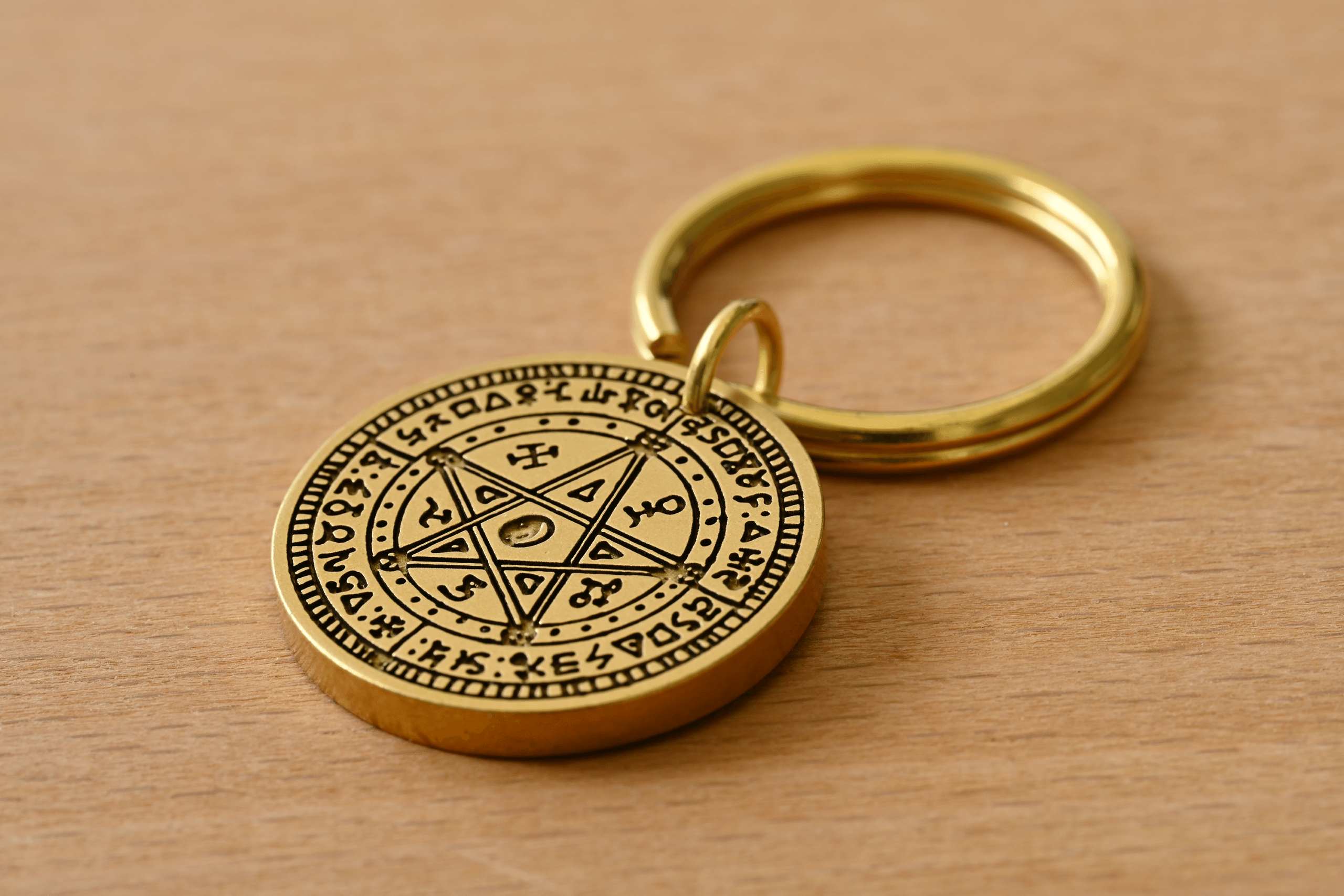 Brass keychain featuring a circular medallion engraved with a pentagram and esoteric symbols on a wooden surface