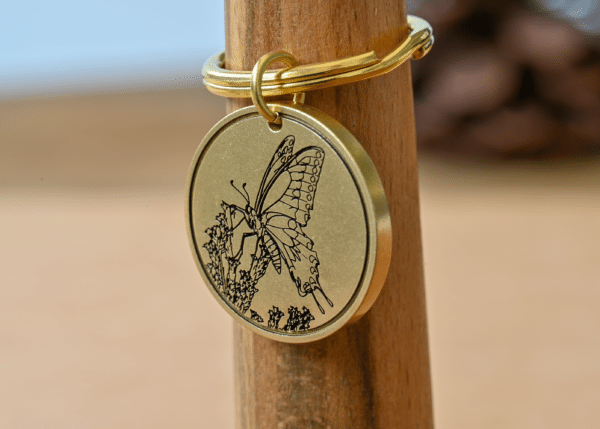Circular brass keychain medallion engraved with a butterfly perching on flowers