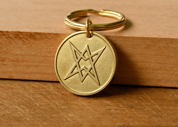 Round brass keychain engraved with a unicursal hexagram symbol resting on a wooden surface