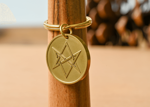 Gold circular keychain tag engraved with a unicursal hexagram hanging on a wooden post