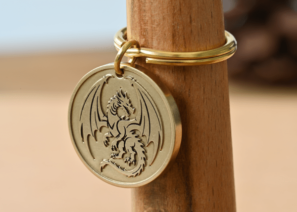 Gold circular brass keychain pendant featuring an engraved dragon with wings spread wide