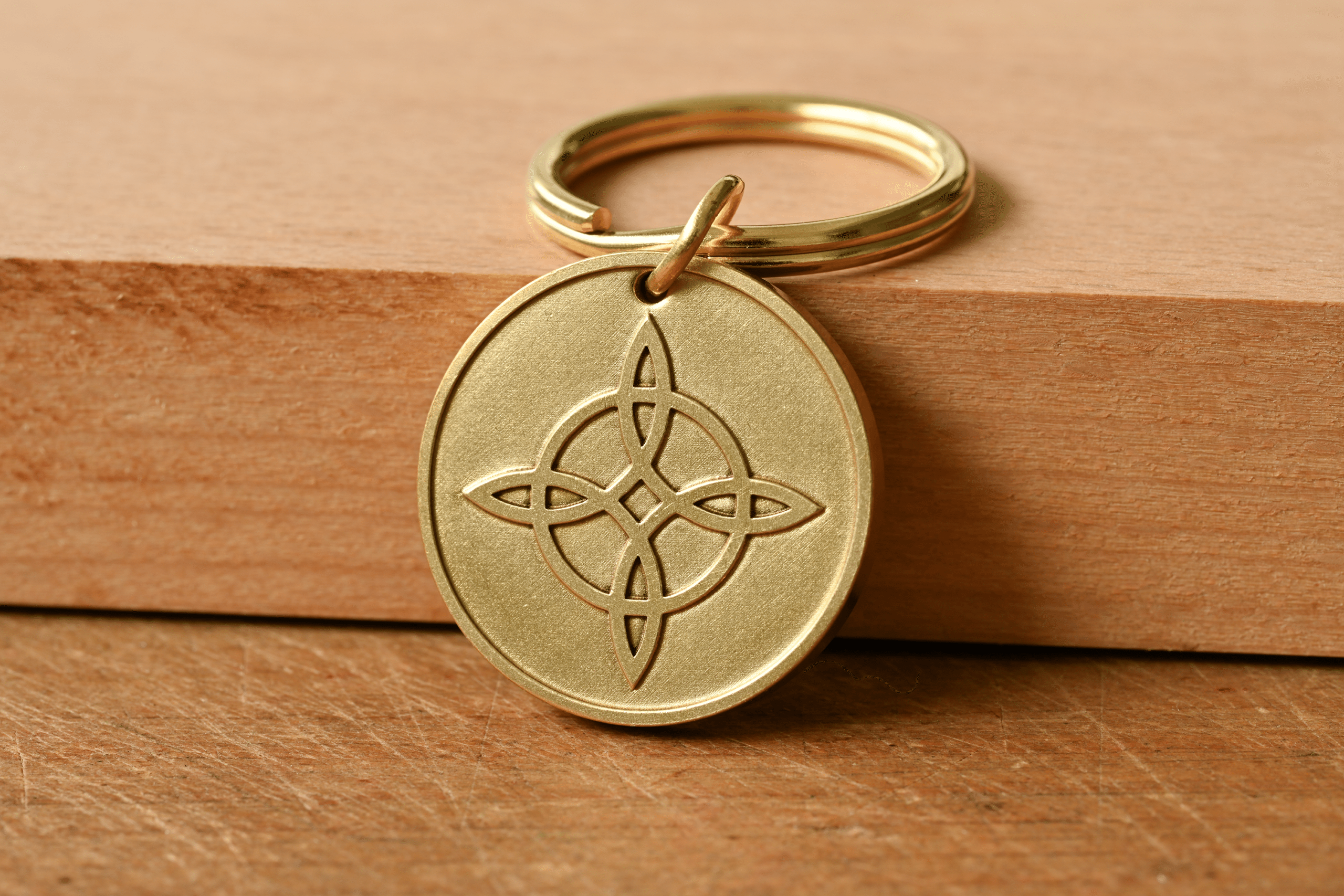 Round brass keychain engraved with a Celtic knot symbol, resting against a wooden block