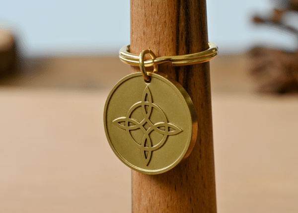 Gold circular keychain tag featuring an engraved witch's knot design