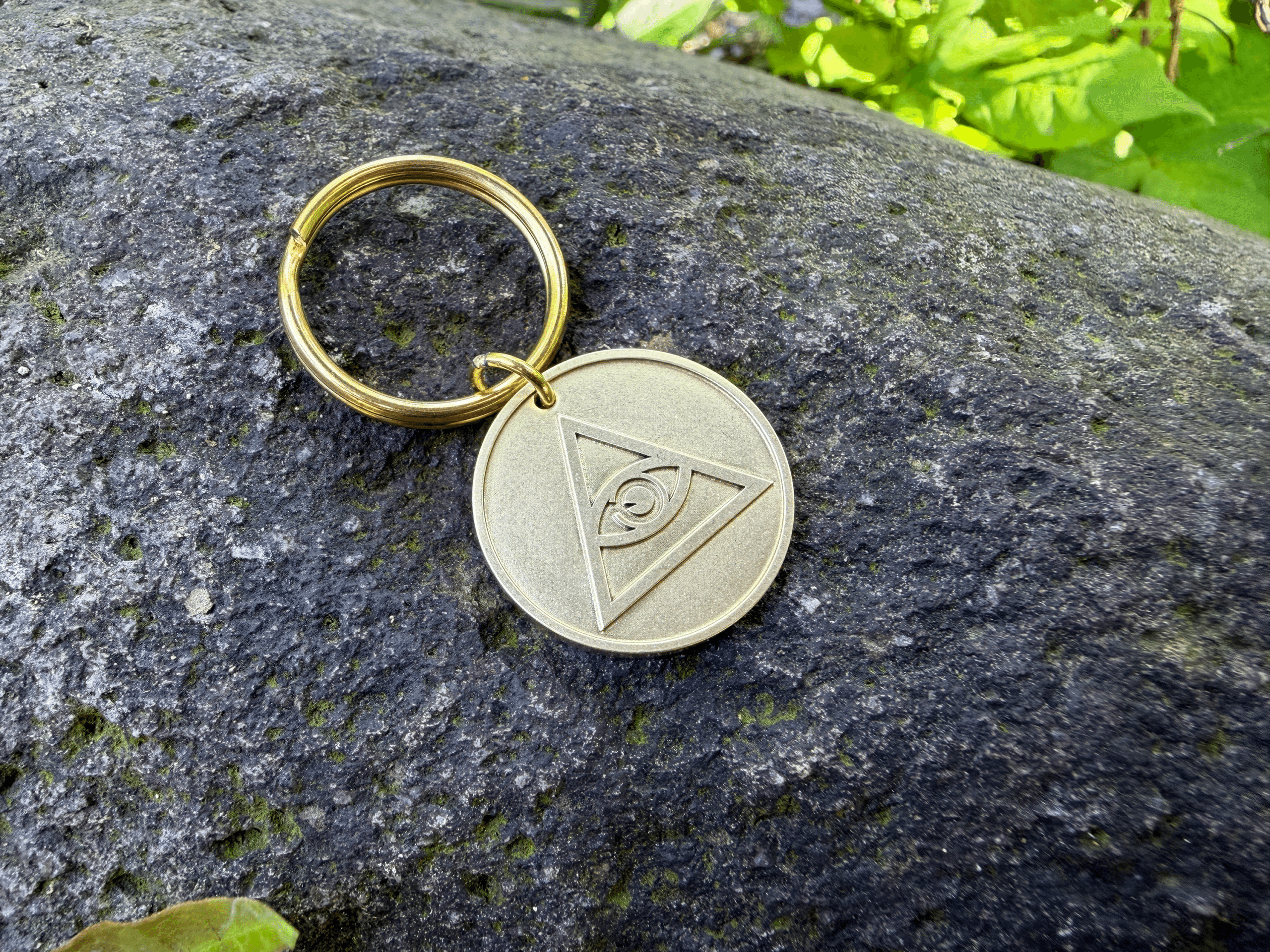 Brass key ring with a round medallion featuring an engraved Eye of Providence, resting on a stone surface