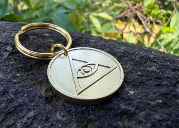 Brass keychain medallion with an engraved Eye of Providence symbol resting on a stone surface